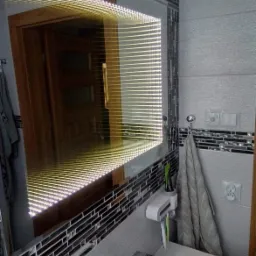 Oświetlone lustro łazienkowe z efektem nieskończoności, obłożone mozaiką, widok na fragment umywalki i akcesoriów łazienkowych.