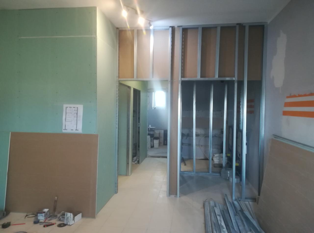 Wnętrze w trakcie montażu ścian działowych z płyt kartonowo-gipsowych na metalowej konstrukcji, widoczne narzędzia i plan pomieszczenia na ścianie.