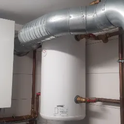 Biała pompa ciepła Panasonic Aquarea z podłączonym zasobnikiem ciepłej wody, instalacją z miedzianych rur i ocynkowanymi kanałami wentylacyjnymi w pomieszczeniu z białymi płytkami.