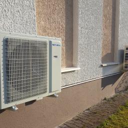 Ekoklimat - Dwa klimatyzatory zewnętrzne marki SEVRA zamontowane na elewacji budynku z ozdobnym tynkiem w pasy, widoczne przewody i kostka brukowa.