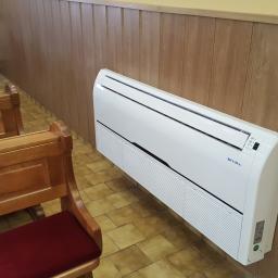 Ekoklimat - Biała jednostka klimatyzacyjna zamontowana na drewnianej ścianie w pomieszczeniu z ławkami. Widoczna marka SEVRA. Drugi, identyczny klimatyzator w tle.