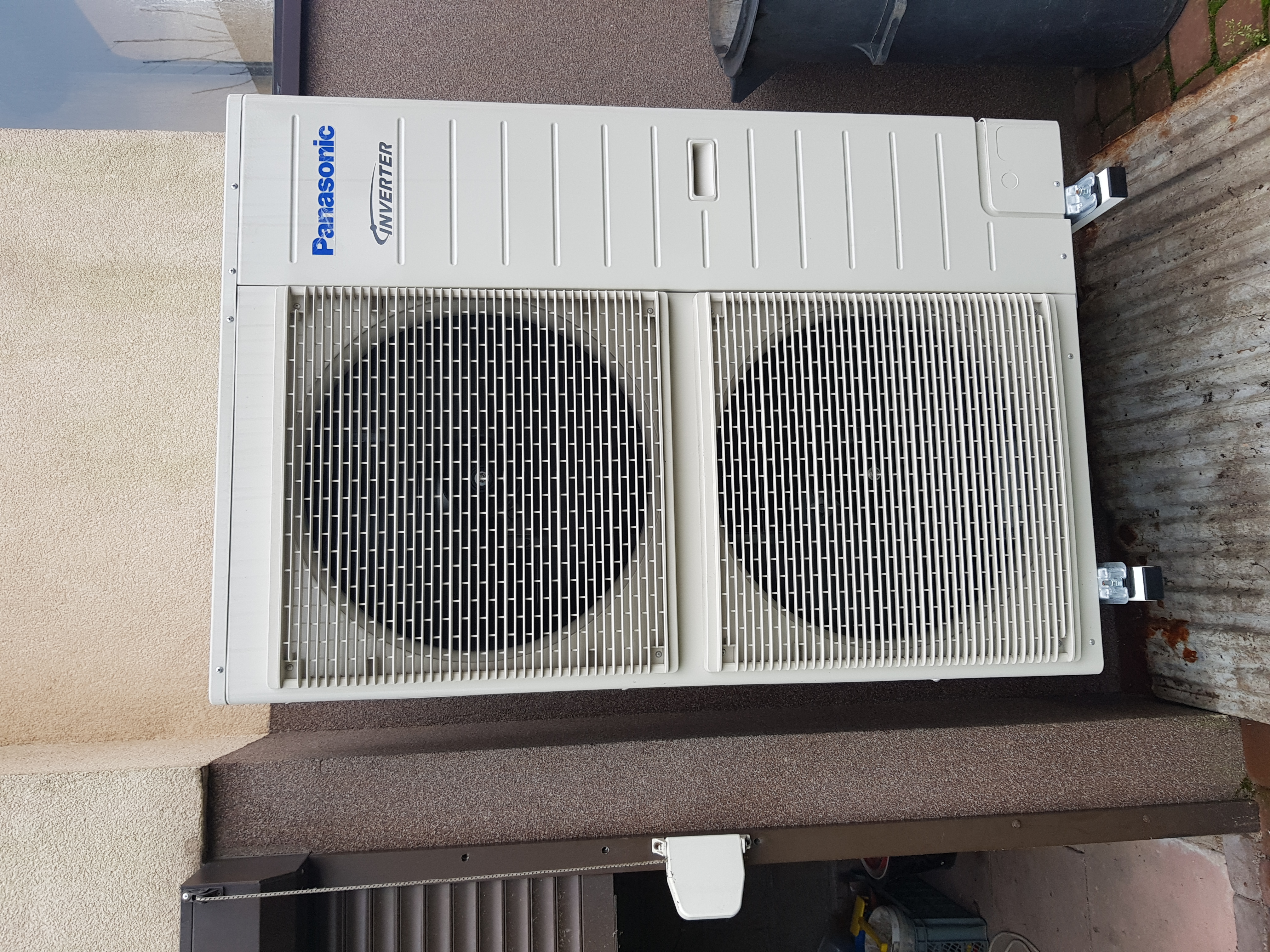 Zewnętrzna jednostka klimatyzacji Panasonic Inverter zamontowana na elewacji budynku, widoczne metalowe uchwyty montażowe.