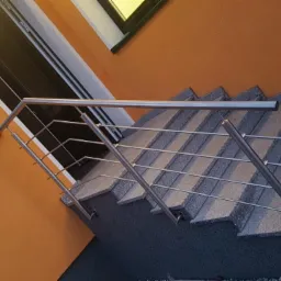 Zewnętrzne schody z szarego kamienia z nowoczesną balustradą ze stali nierdzewnej, widok z dołu, pomarańczowa elewacja budynku w tle.