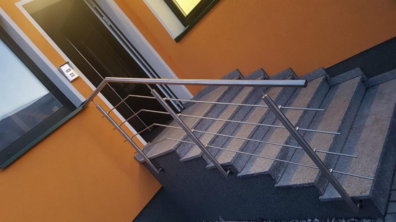 Zewnętrzne schody z szarego kamienia z nowoczesną balustradą ze stali nierdzewnej, widok z dołu, pomarańczowa elewacja budynku w tle.