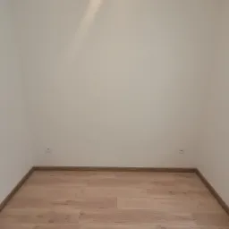 Pusty pokój po remoncie z nową podłogą z paneli drewnopodobnych i świeżo pomalowanymi na biało ścianami z widocznymi dwoma gniazdkami elektrycznymi.