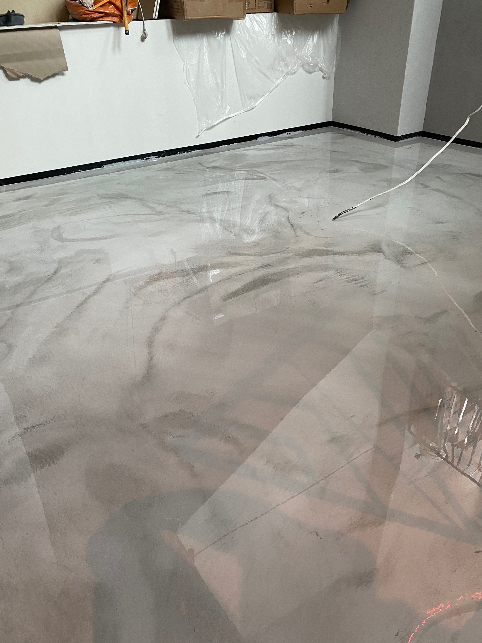 Błyszcząca, szara podłoga z efektem marmuru, świeżo wylana, z widocznymi refleksami światła i czarną listwą przypodłogową.