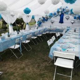 Dekoracja namiotu na przyjęcie urodzinowe z niebieskimi i białymi balonami, pomponami i stołami nakrytymi w błękitnej kolorystyce.