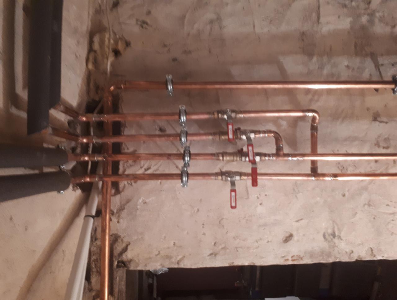Miedziane rury z zaworami zamontowane na surowej ścianie. Widoczne elementy instalacji, obejmy mocujące i izolacja termiczna rur.
