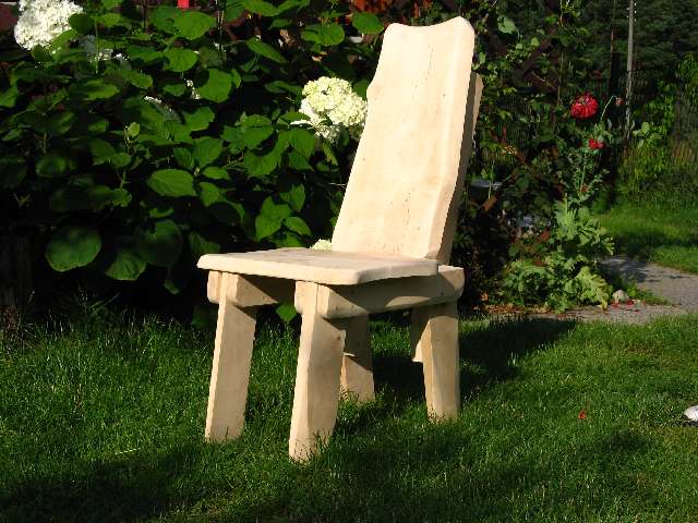 Drewniane krzesło ogrodowe o surowym wykończeniu, ustawione na trawie przed kwitnącymi krzewami hortensji i różami.