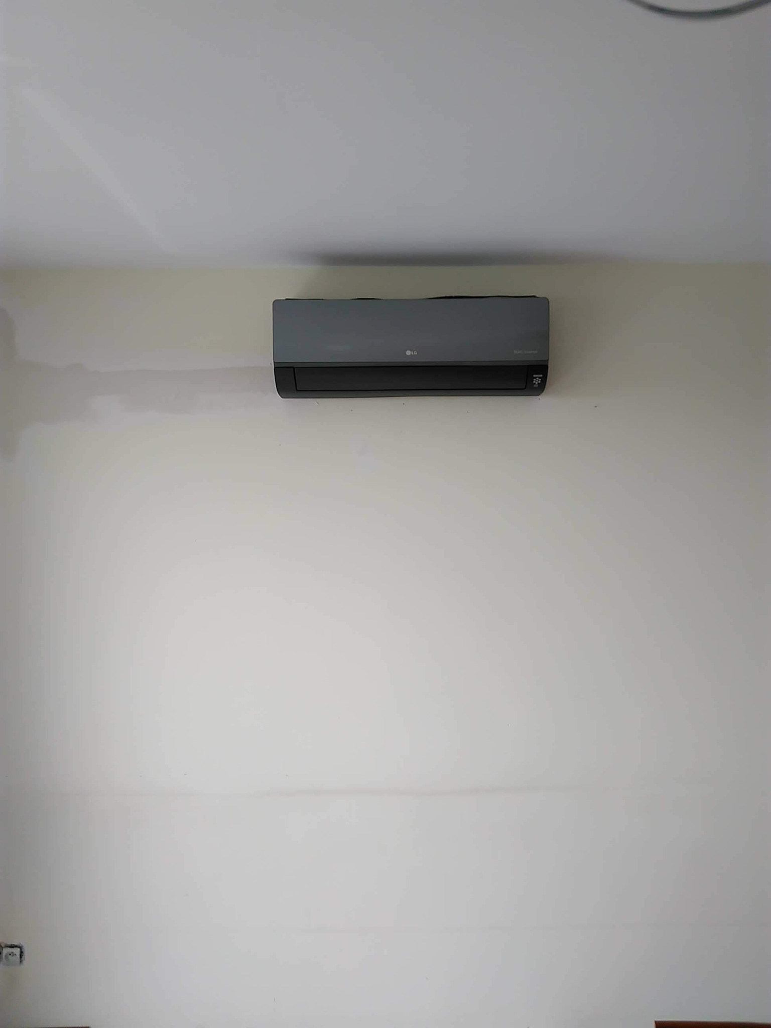 Szary klimatyzator LG zamontowany na białej ścianie z widocznymi śladami po szpachlowaniu.