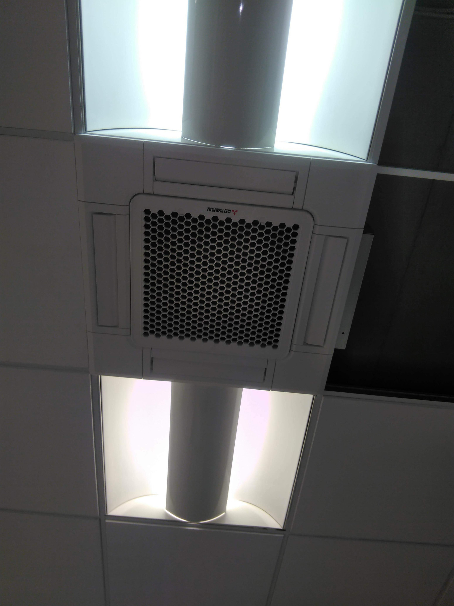 Sufitowa kaseta klimatyzacyjna marki Mitsubishi, zamontowana w podwieszanym suficie z oświetleniem kasetonowym.