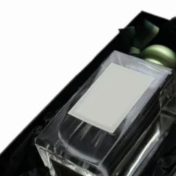 Elegancki flakon perfum z pustą etykietą w czarnym, teksturowanym pudełku prezentowym, widoczne zielone akcenty dekoracyjne.