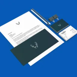 Makieta identyfikacji wizualnej firmy z logo na papierze firmowym, wizytówce i teczce, ułożona na niebieskim tle z ołówkami i klipsami.