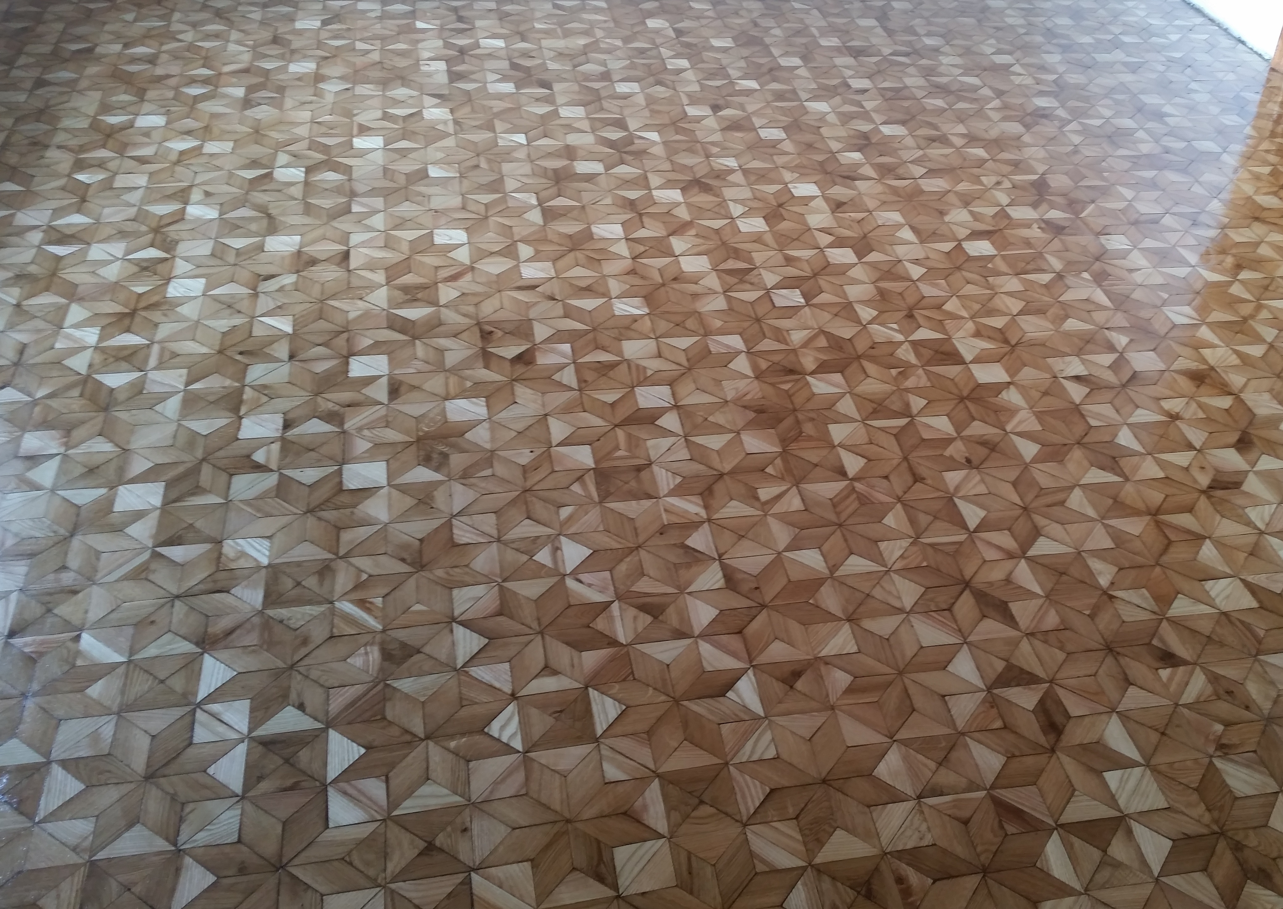 Parkiet ułożony w geometryczny wzór gwiazd, z wyraźnymi słojami drewna i delikatnym połyskiem lakieru.