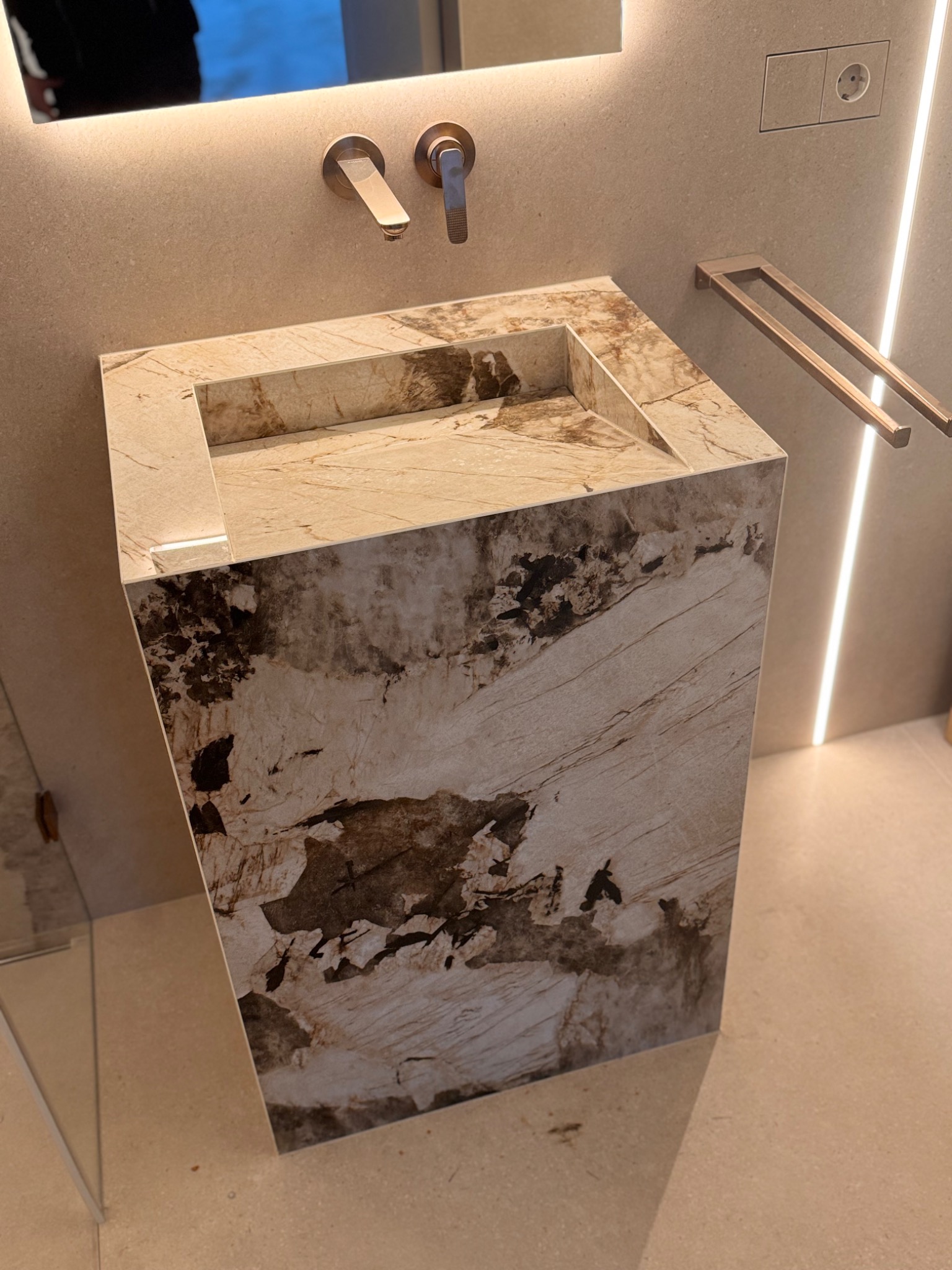 Beżowa umywalka wolnostojąca z marmurowym wzorem, nowoczesna armatura, oświetlenie LED i minimalistyczny wieszak na ręczniki w wykończonej łazience.