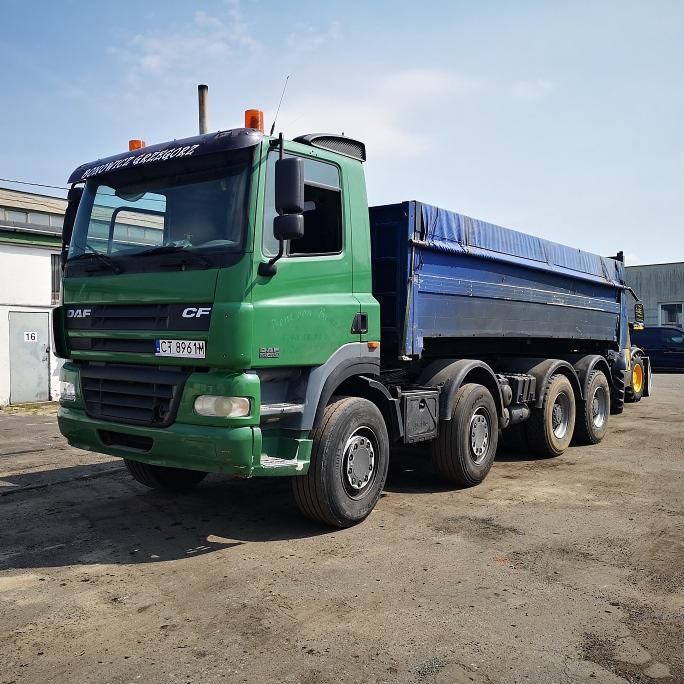 Zielona ciężarówka DAF CF z niebieską plandeką na naczepie, zaparkowana na placu budowy, widoczny numer rejestracyjny CT 8961M.