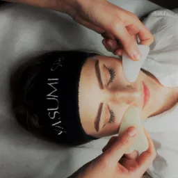 Kobieta z zamkniętymi oczami podczas zabiegu z użyciem kamieni Gua Sha, czarna opaska Yasumi SPA na włosach.