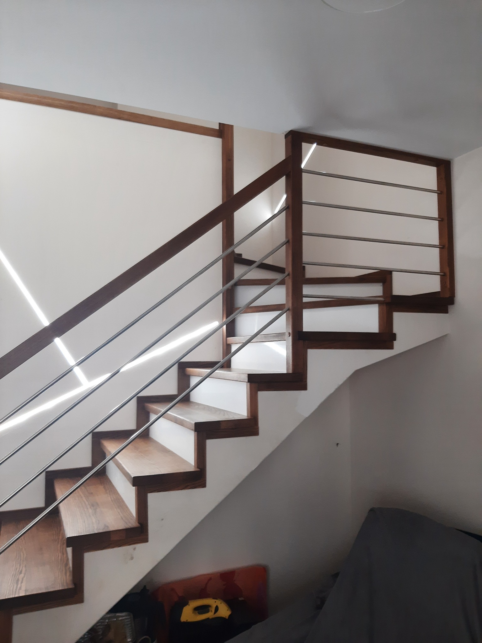 Drewniane schody z metalowymi poręczami w nowoczesnym wnętrzu, oświetlone promieniami światła padającymi z góry.