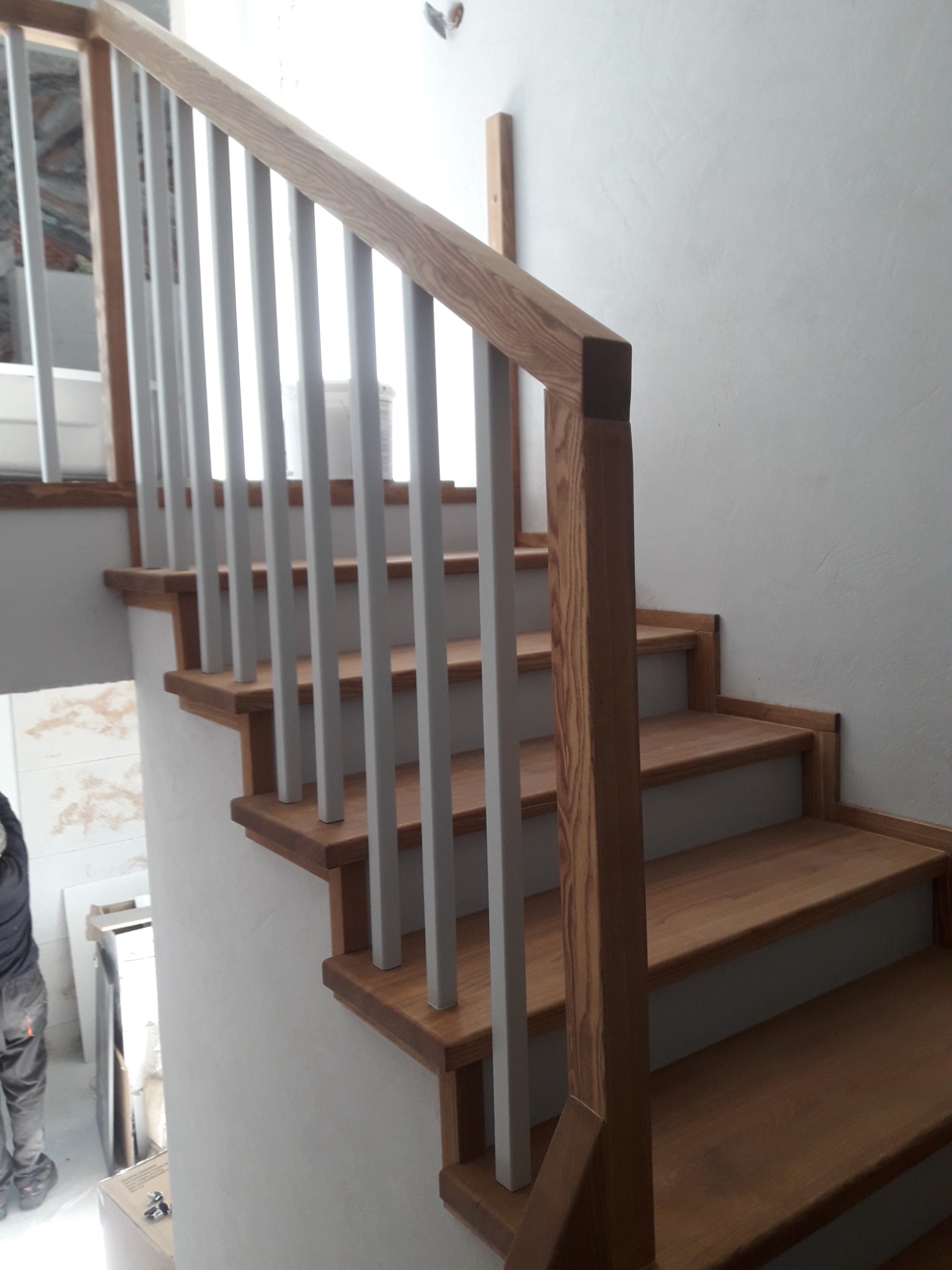 Drewniane schody z jasnymi poręczami z pionowych słupków, wykończone w naturalnym odcieniu drewna, widok z dołu na wznoszące się schody.