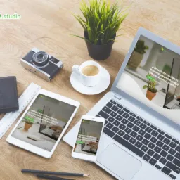 Laptop, tablet i smartfon wyświetlają identyczną stronę internetową firmy Naxe.studio, obok filiżanka kawy, roślina doniczkowa i akcesoria biurowe na drewnianym biurku.