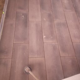 Artur - Ułożona, brązowa kostka o wyraźnym rysunku drewna, widoczny gumowy młotek do dobijania kostki brukowej oraz poziomica i fragment białego materiału izolacyjnego.