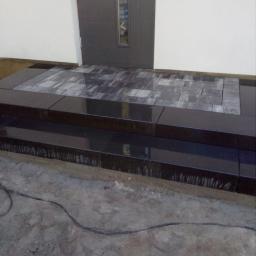 Artur - Schody wejściowe do domu wyłożone ciemną kostką granitową, z widocznymi śladami zaprawy na krawędziach i niezagospodarowanym terenem wokół.