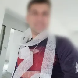 Mężczyzna z taśmą malarską na ubraniu, w tle surowe, białe ściany w trakcie remontu. Widoczne ślady farby na ubraniu.