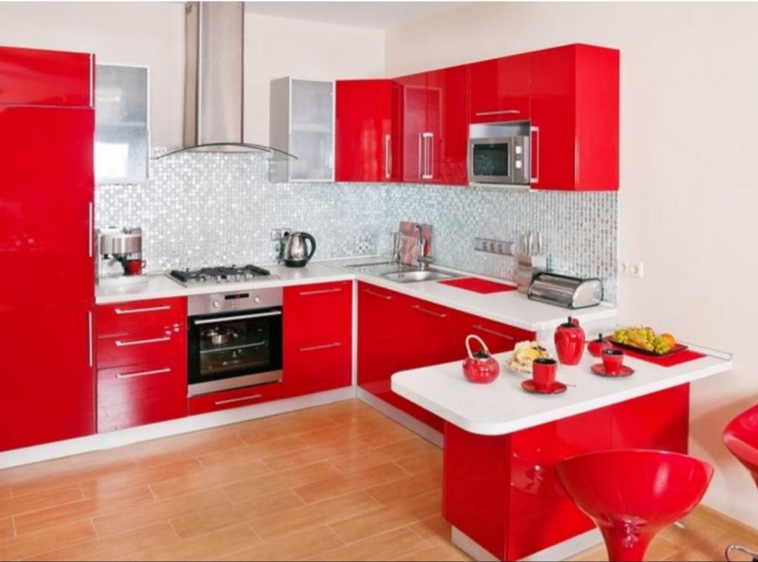 Nowoczesna kuchnia z błyszczącymi, czerwonymi frontami szafek, mozaiką na ścianie i drewnianą podłogą. Na blacie ekspres do kawy, czajnik i toster.