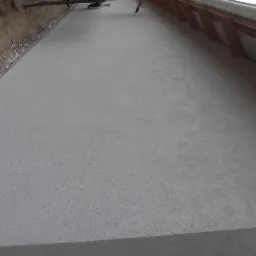 Świeżo otynkowana szara elewacja budynku w trakcie prac wykończeniowych, widoczne krokwie dachu oraz narzędzia pracy na górze kadru.