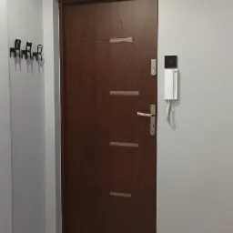 Szare ściany przedpokoju z ciemnymi drzwiami wejściowymi, biała listwa przypodłogowa i podłoga z białego marmuru.