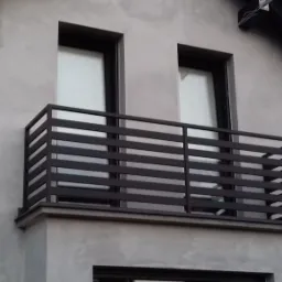 Balkon z nowoczesną, prostą balustradą w kolorze ciemnego grafitu, widok z dołu na tle szarej elewacji domu z dwoma oknami.