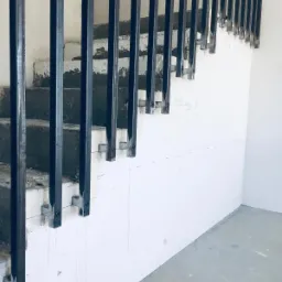 Montaż metalowych słupków pionowych do schodów betonowych, przygotowanie do instalacji barierki, widoczne ślady po wierceniu i brud na stopniach.