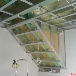 Szkielet metalowy pod zabudowę poddasza z izolacją z wełny mineralnej, widoczny fragment drabiny i narzędzia do cięcia profili.