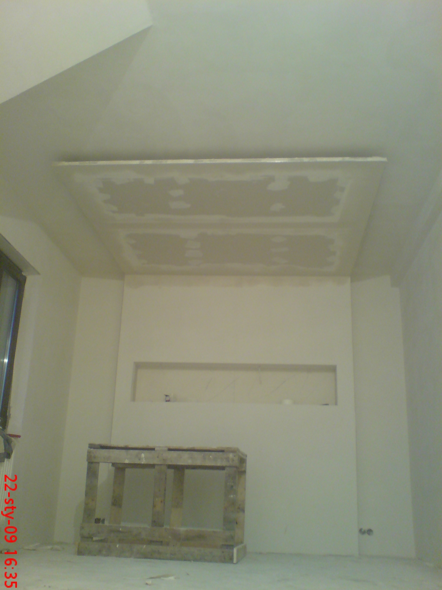 Poddasze w trakcie zabudowy: widoczny sufit z wykończeniem gipsowym, ściany przygotowane do malowania i drewniany stelaż na podłodze.