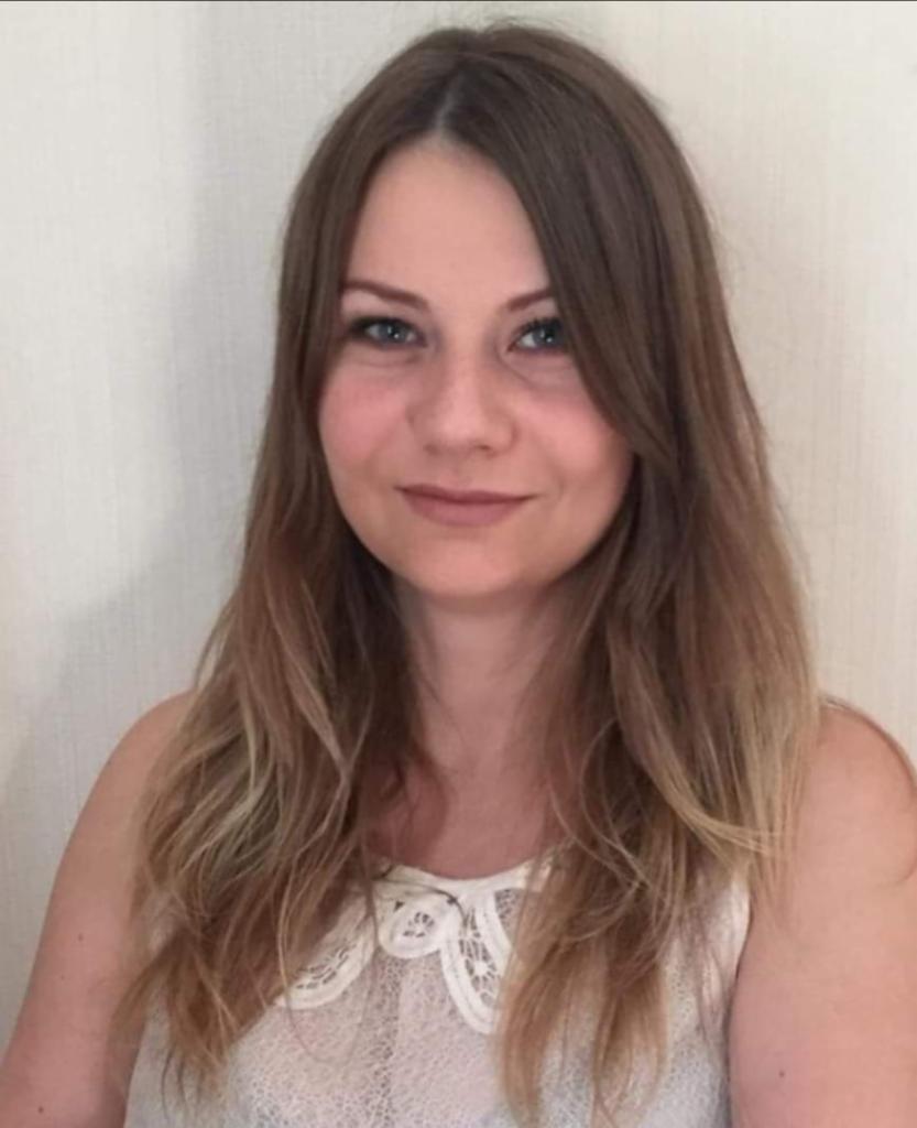 Portret kobiety z długimi, brązowymi włosami i koronkowym kołnierzykiem, uśmiechająca się subtelnie w kierunku kamery.