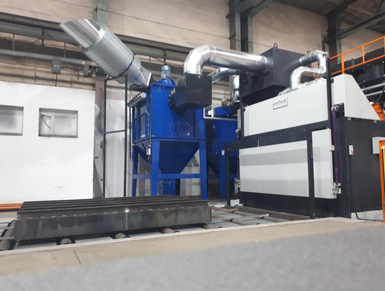 Przemysłowa linia do obróbki powierzchni metalu, z widoczną kabiną roboczą, systemem filtracji powietrza i transportem rolkowym dla elementów stalowych.