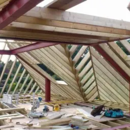 Konstrukcja drewnianej więźby dachowej z elementami stalowymi, widok z wnętrza poddasza, narzędzia pracy na podłodze.