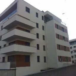 Nowoczesny budynek wielorodzinny z białymi elewacjami i drewnianymi akcentami na balkonach i elewacji, widok z dołu na dwa budynki.