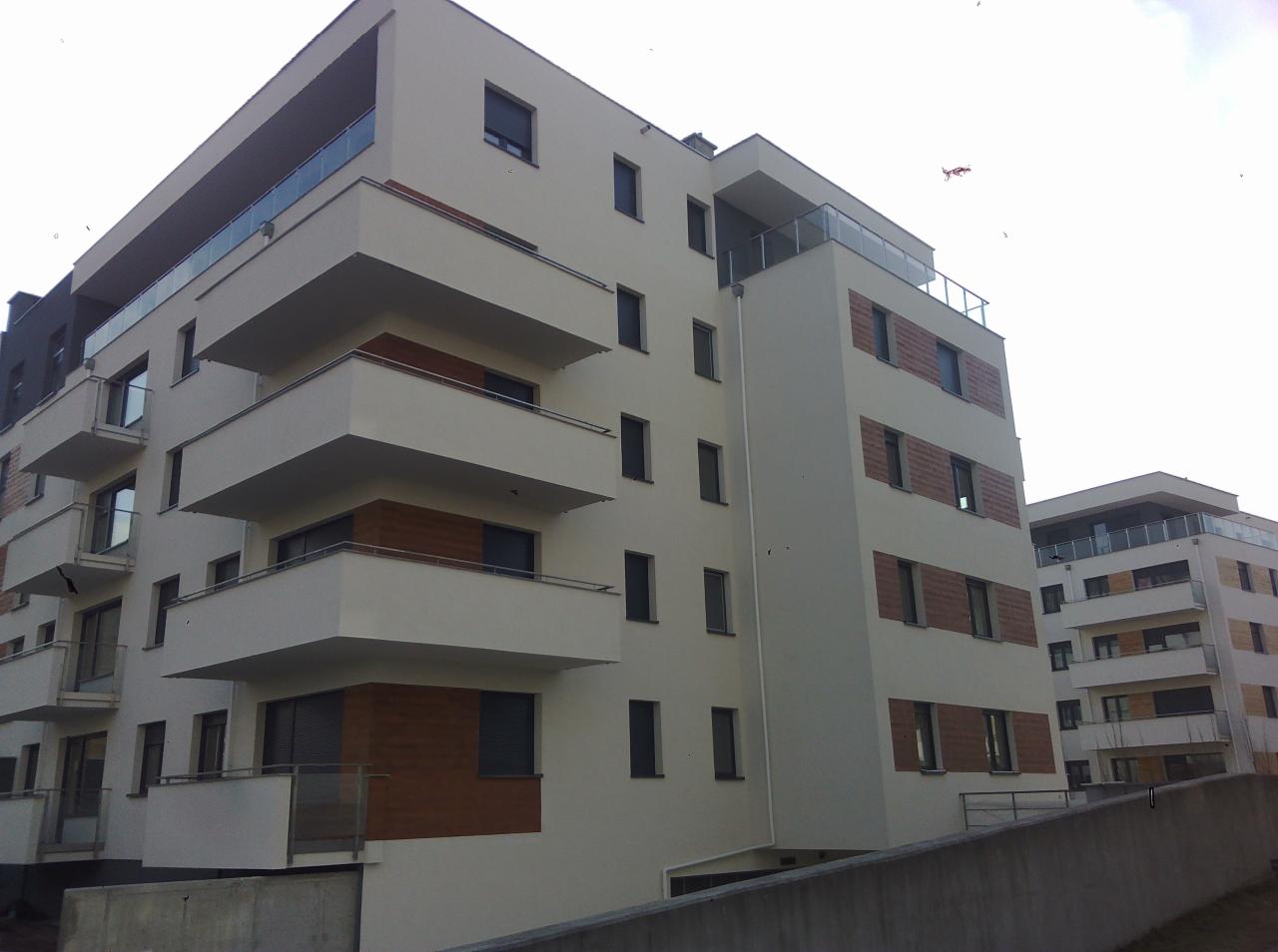 Nowoczesny budynek wielorodzinny z białymi elewacjami i drewnianymi akcentami na balkonach i elewacji, widok z dołu na dwa budynki.