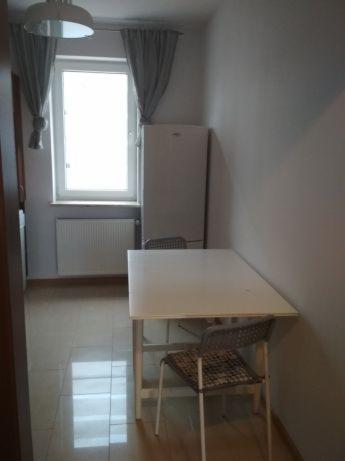 Wnętrze pokoju po odświeżeniu, z widocznymi świeżo pomalowanymi ścianami w jasnym odcieniu, białym stołem i krzesłami, oraz oknem z szarymi zasłonami.