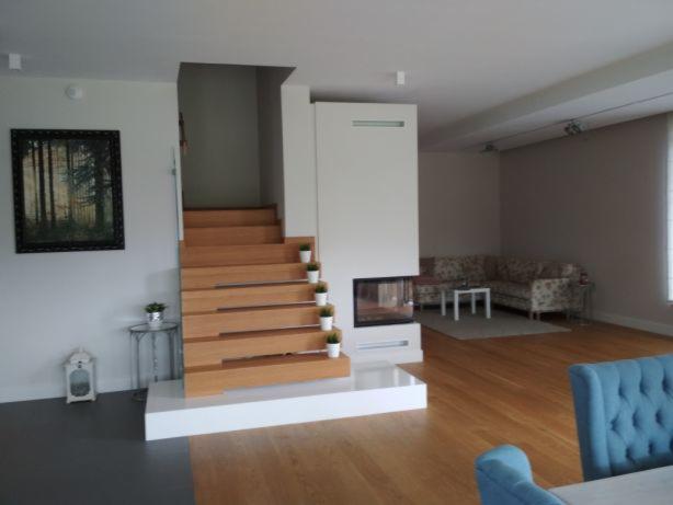 Jasne wnętrze pokoju dziennego z drewnianymi schodami ozdobionymi małymi doniczkami, nowoczesnym kominkiem i sofą w kwiaty w tle.