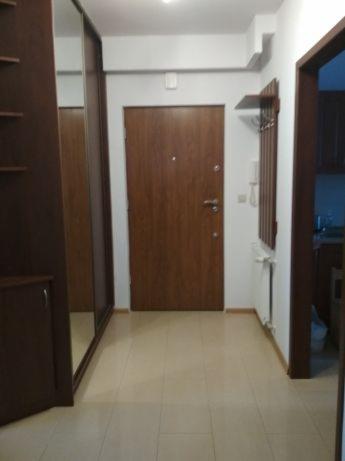 Przedpokój po odświeżeniu: nowa, ciemnobrązowa stolarka drzwiowa i odmalowane ściany na biało, widoczny grzejnik i wieszak z półką.