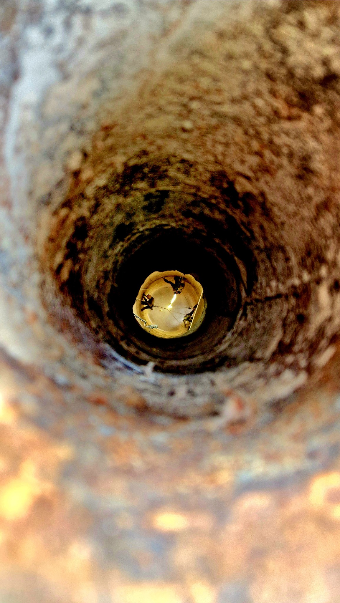 Wnętrze komina z cegły w Katowicach widziane od dołu, z linami i sprzętem zabezpieczającym na górze, sugerujące prace wysokościowe.