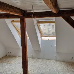 Poddasze po remoncie z drewnianymi belkami, oknami dachowymi i przygotowaną podłogą z płyt OSB oraz wyprowadzonymi instalacjami elektrycznymi.
