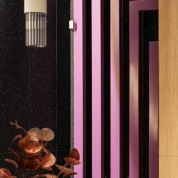 Ambiente Dominika Cymerman - Nowoczesna łazienka: czarne płytki z brokatem, różowy grzejnik dekoracyjny, designerska lampa i brązowe liście w wazonie. Minimalistyczny, ale wyrazisty detal.