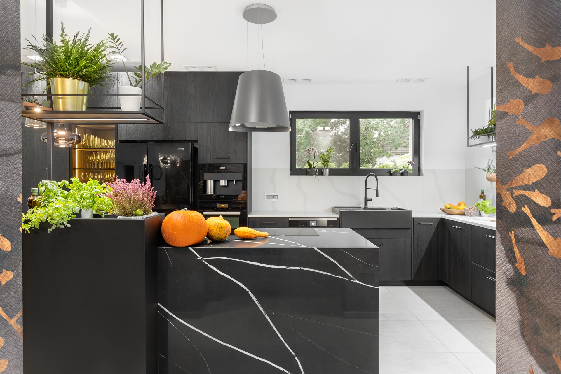 Nowoczesna kuchnia w odcieniach szarości i czerni z wyspą z czarnego marmuru, dyniami i ziołami. Minimalistyczny design z akcentami roślinnymi i naturalnym światłem.