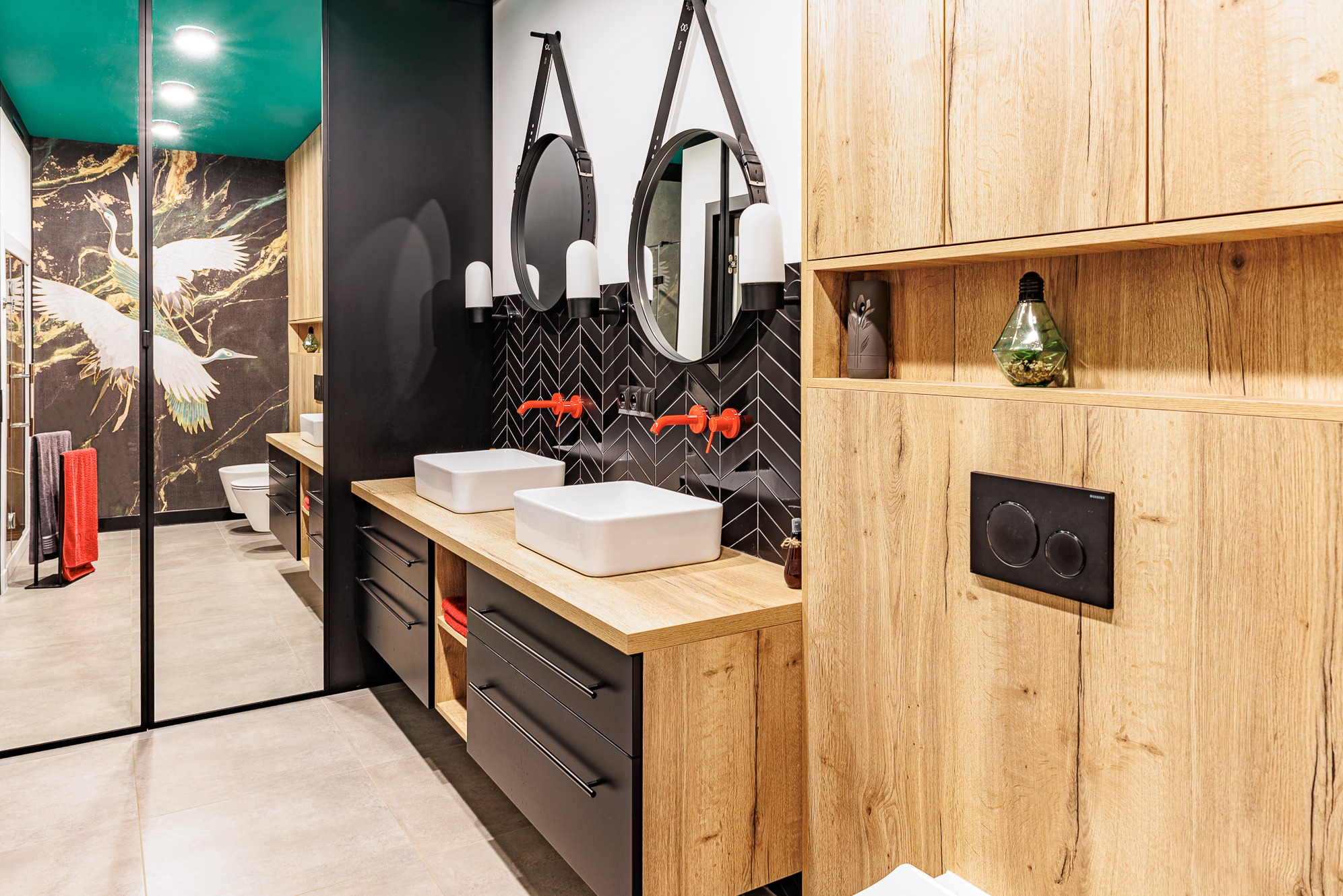 Nowoczesna łazienka w Zabrzu: Dwie białe umywalki na drewnianym blacie, czarne szafki, okrągłe lustra na paskach i czarne płytki w jodełkę. Akcenty kolorystyczne: czerwone krany.
