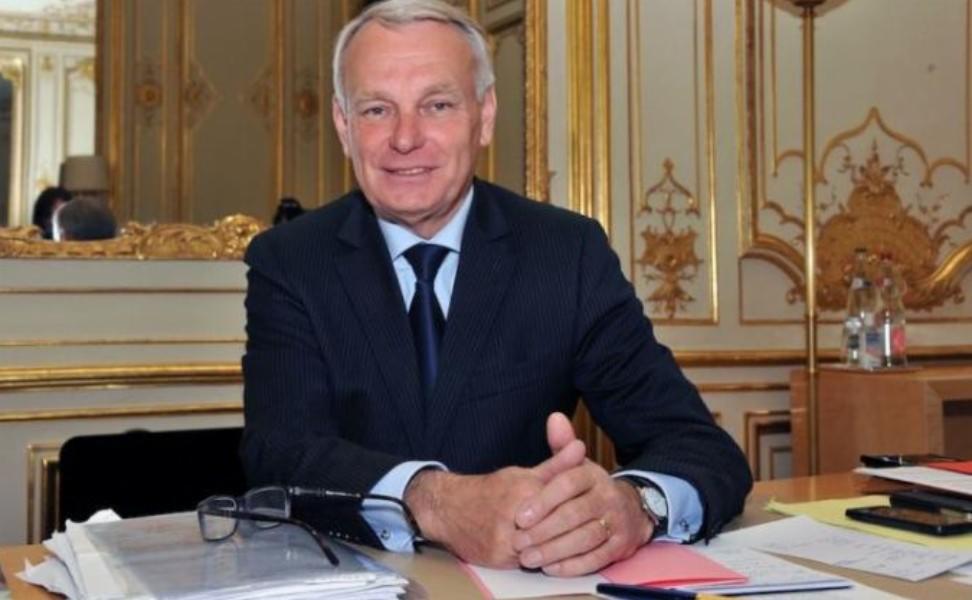 Portret mężczyzny w garniturze, siedzącego za biurkiem z dokumentami i okularami. W tle bogato zdobione wnętrze z elementami złota.