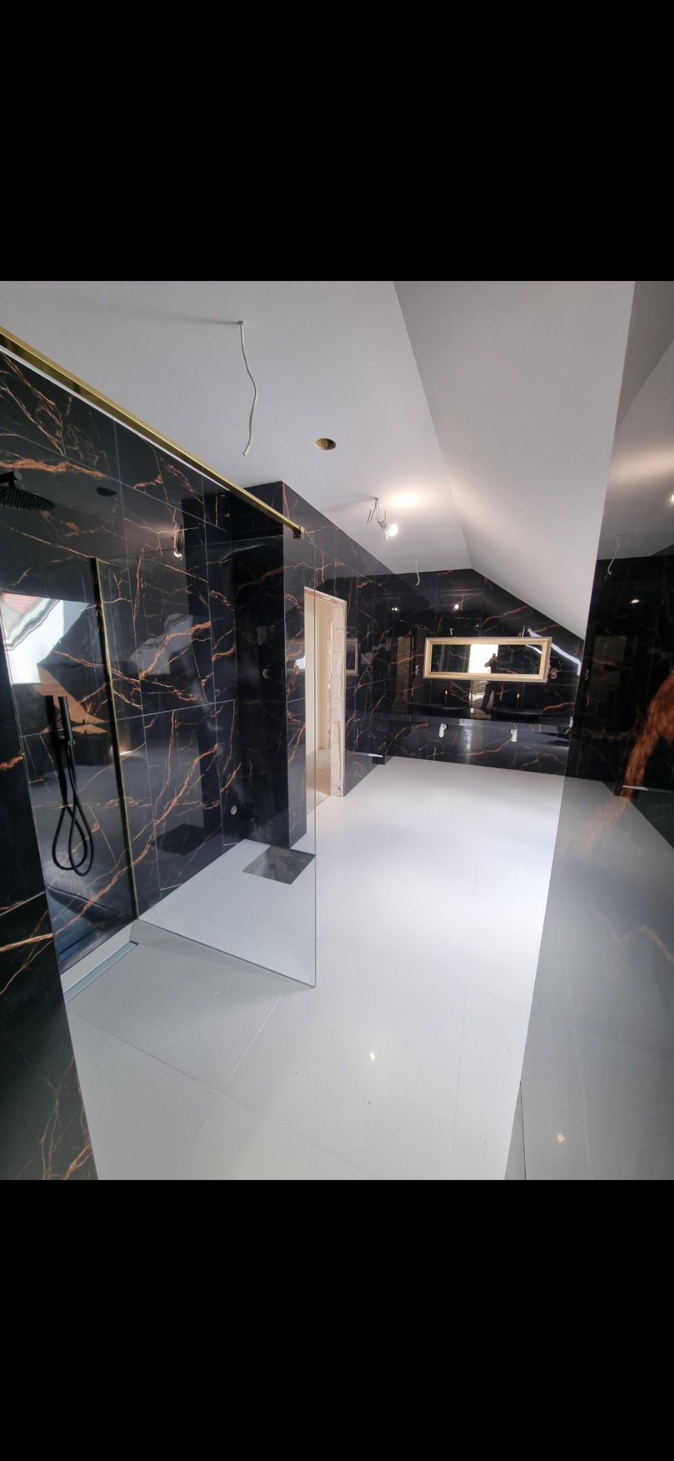 Nowoczesna łazienka na poddaszu z czarnymi płytkami imitującymi marmur z złotymi żyłami, białą podłogą z płytek, szklaną kabiną prysznicową typu walk-in i podwieszaną szafką z lustrem.