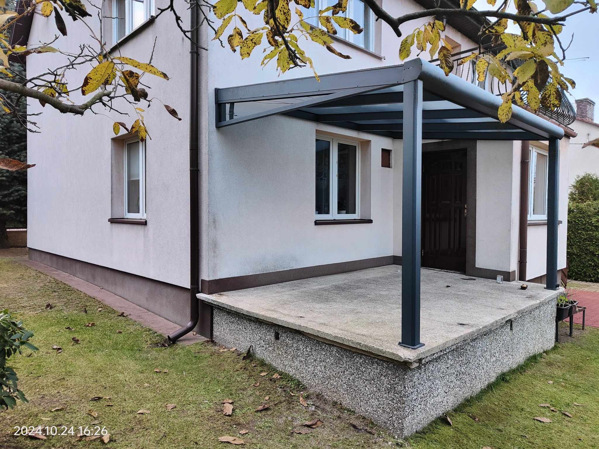Metalowa konstrukcja zadaszenia tarasu przy domu jednorodzinnym, widok z boku, jesienne liście na pierwszym planie.